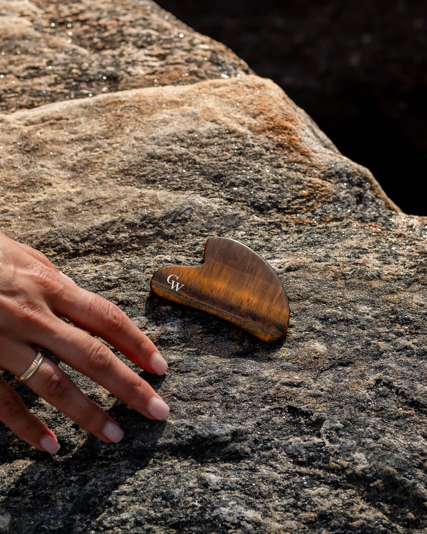 The Gua Sha by Cacti Wellness next to a hand on a rock by the ocean